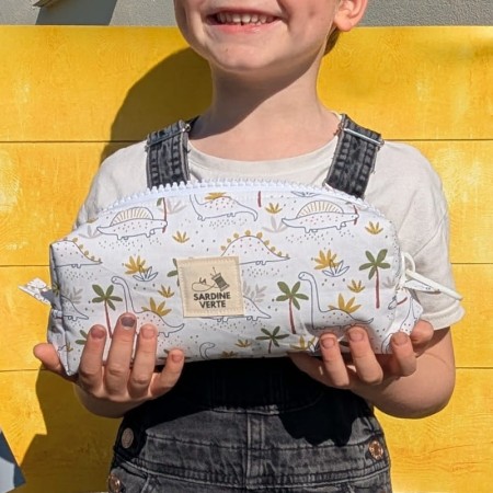 Enfant tenant dans ses mains la trousse à colorier au fond blanc avec des dinosaures
