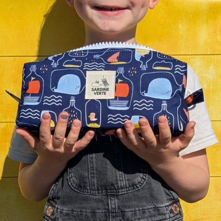Enfant tenant dans ses mains une trousses à colorier aux motifs de bouteilles à la mer sur fond bleu marine